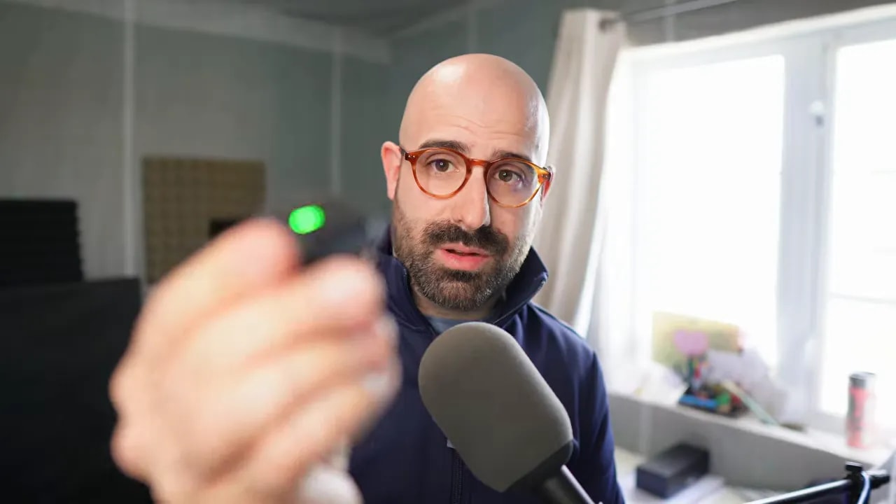 Tiny black recorder held close to camera with green status light visible