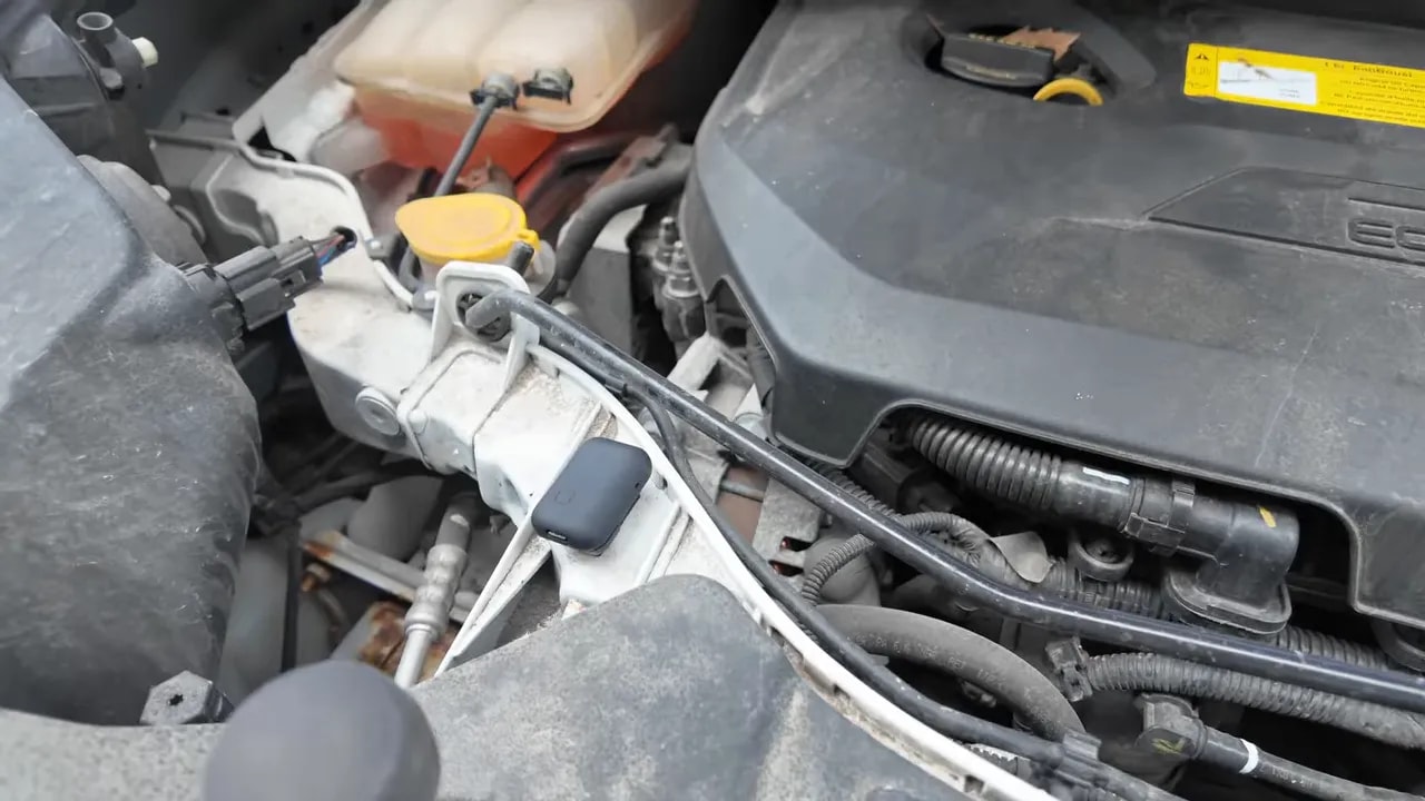 Open car engine bay with recorder positioned near engine components