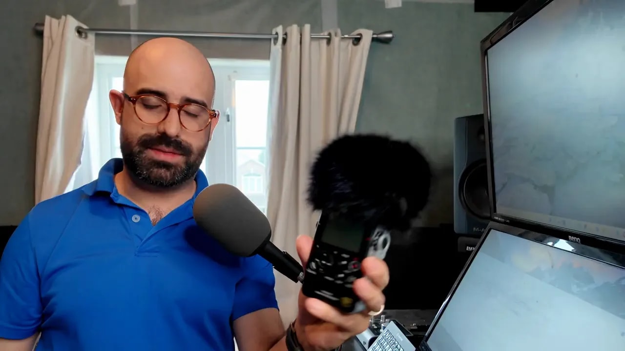 Handheld recorder with black furry wind protection attached over its microphones