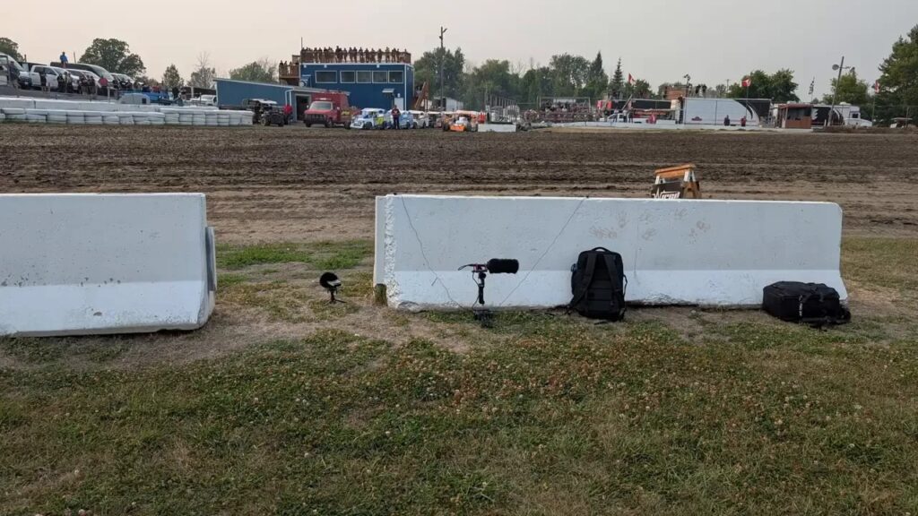 Microphones placed near white barriers beside a dirt oval race track