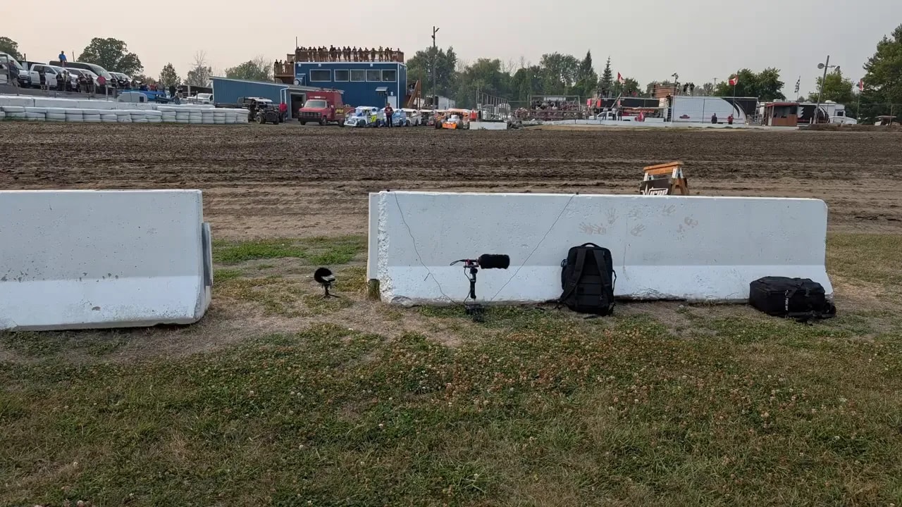 Microphones placed near white barriers beside a dirt oval race track